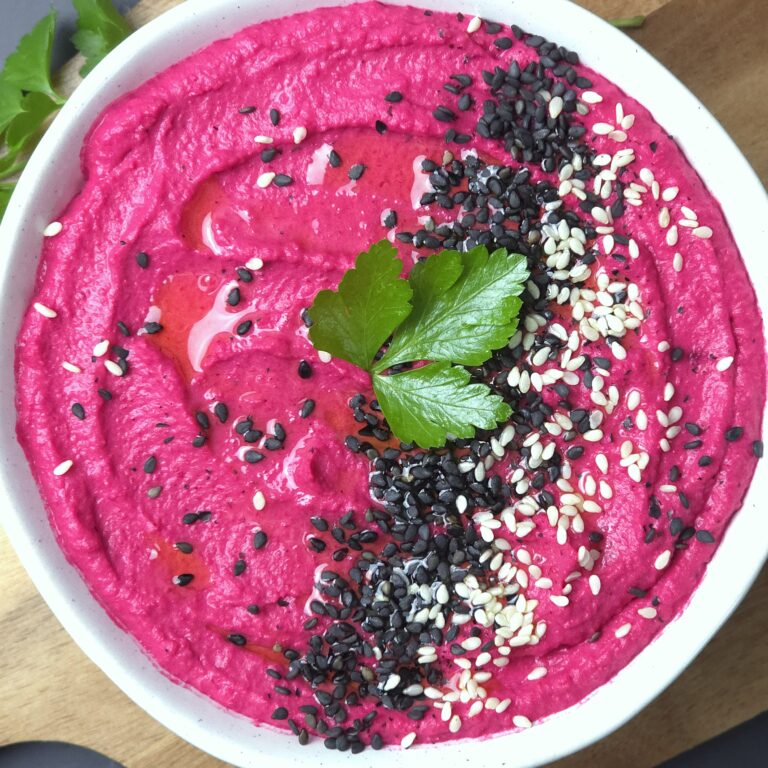 beetroot hummus recipe in a white stoneware bowl, sprinkled with black and white sesame seeds
