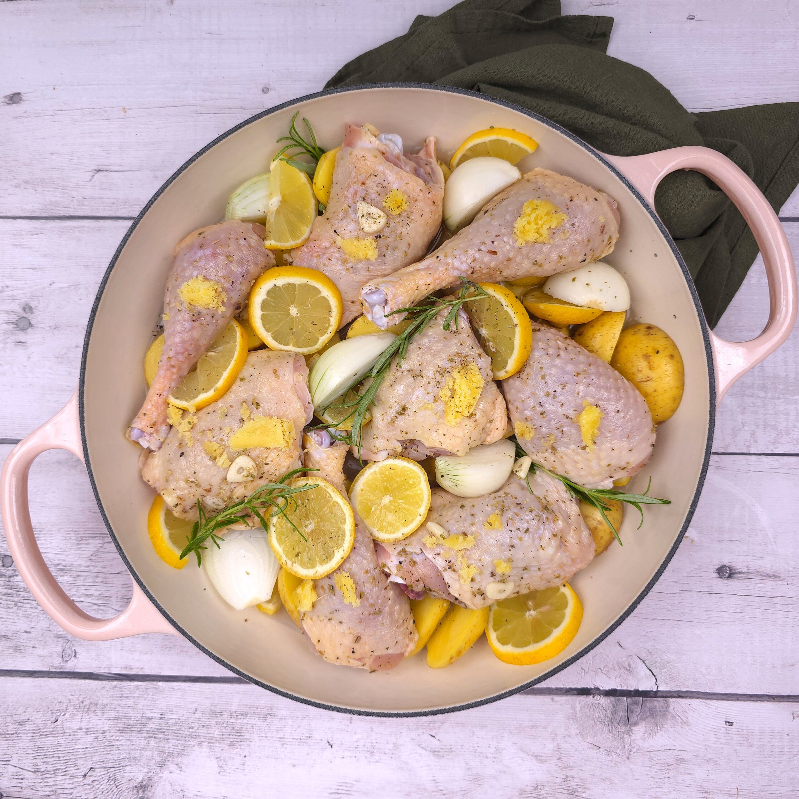 raw Greek chicken thighs and halved potatoes arranged in a cast iron casserole before baking