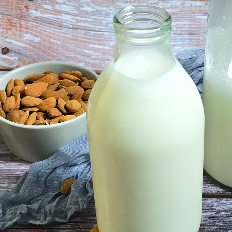 a bottle with homemade almond milk next to a bowl with almonds