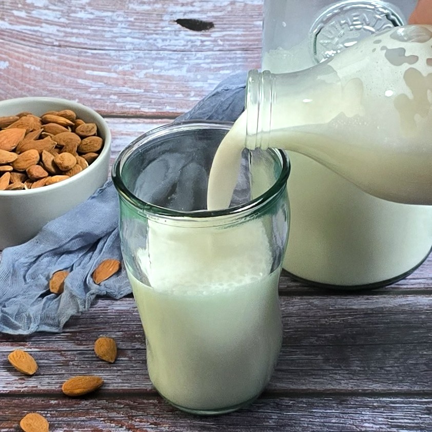 pouring almond milk from bottle to a glass next to a bowl with almonds