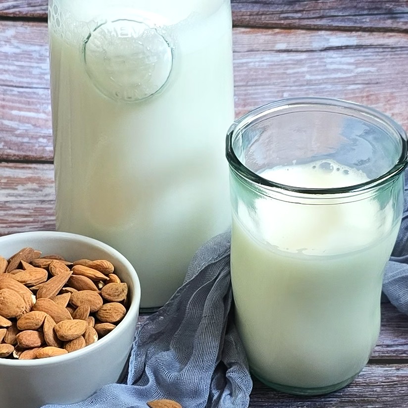 a bottle and glass with almond milk next to a bowl with almonds