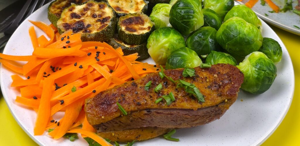 two plates with crispy roasted duck breasts with sides of steamed Brussel sprouts, roasted courgettes, carrots salad and avocado dip