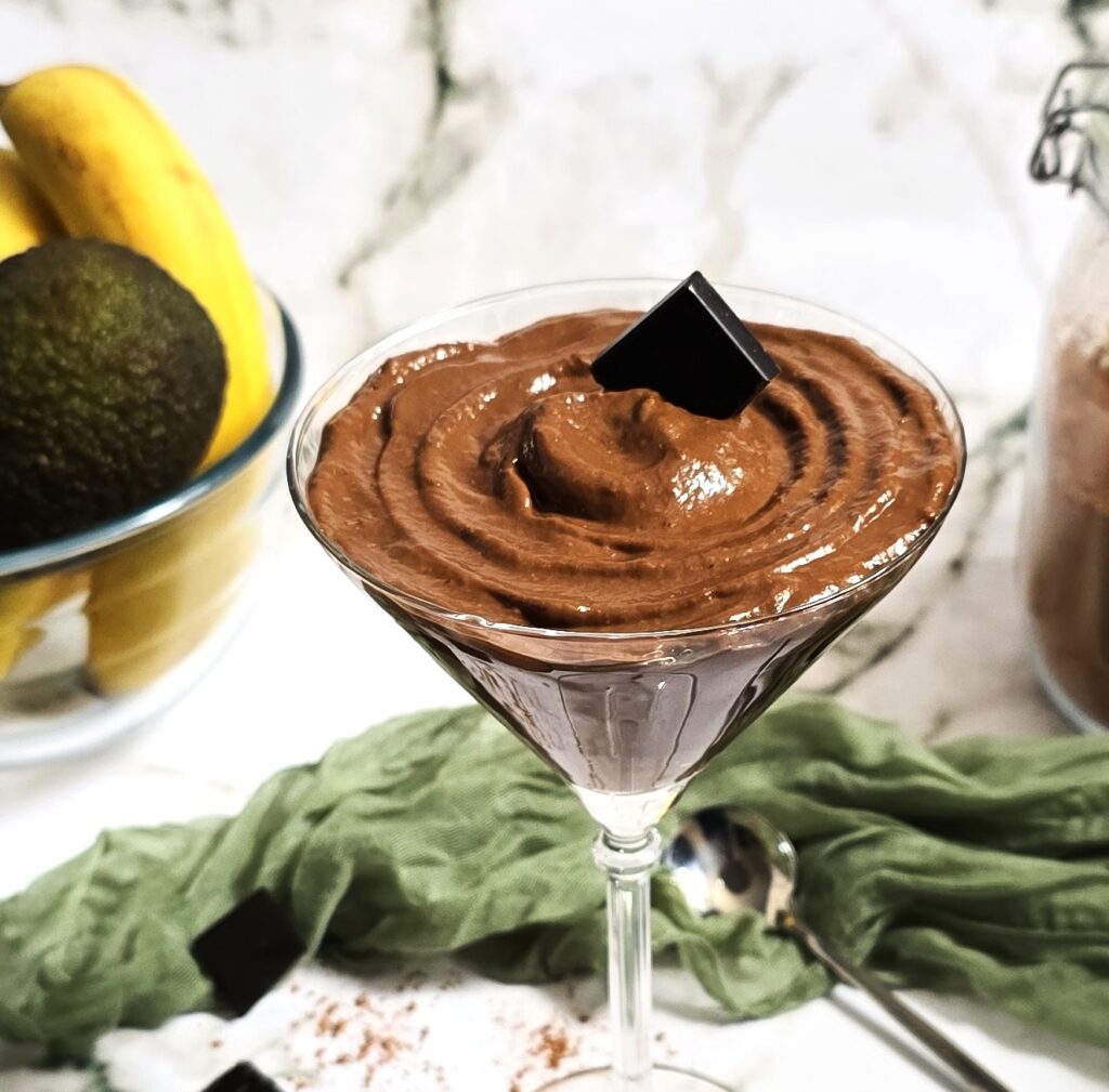 Glass bowl with creamy avocado chocolate mousse, topped with block dark chocolate.