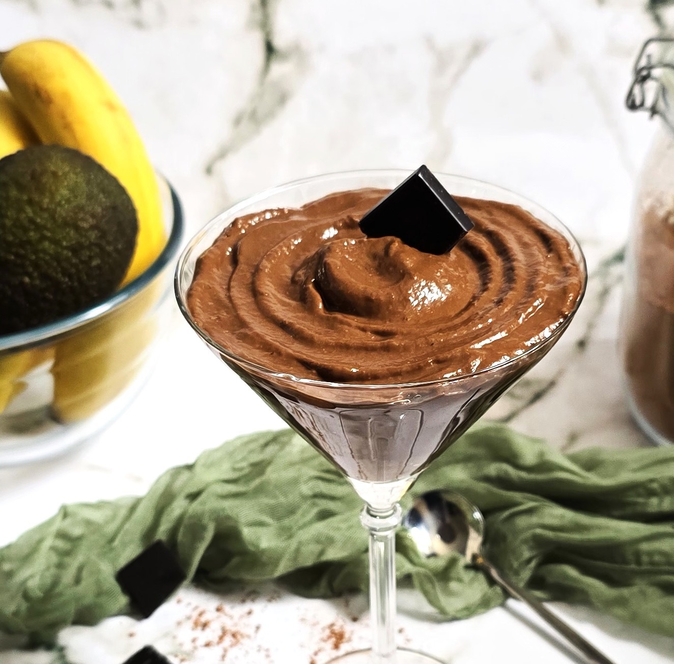 Glass bowl with creamy chocolate avocado mousse, topped with block dark chocolate.