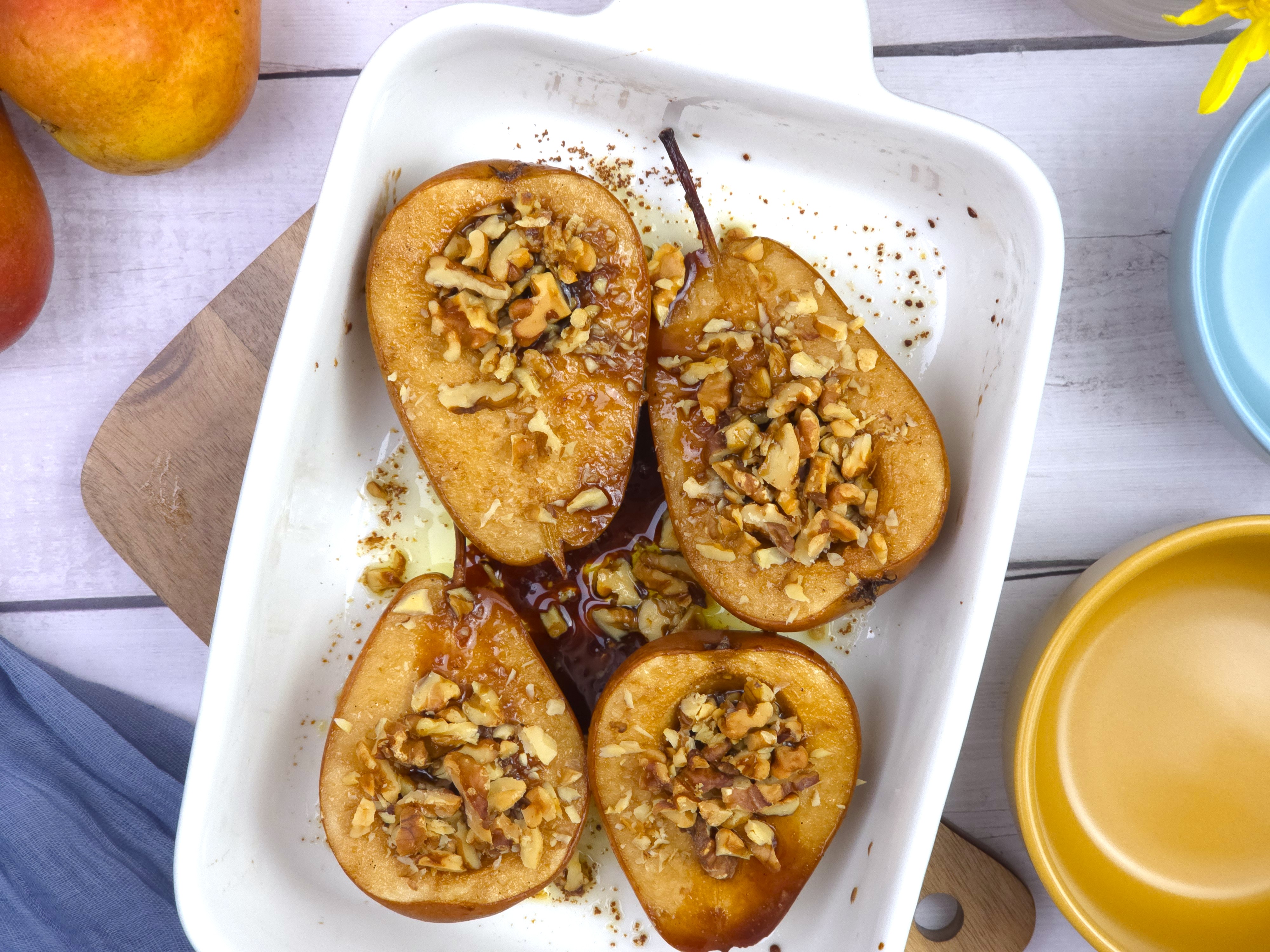 a white ceramic baking dish with roasted pears with crushed walnut topping
