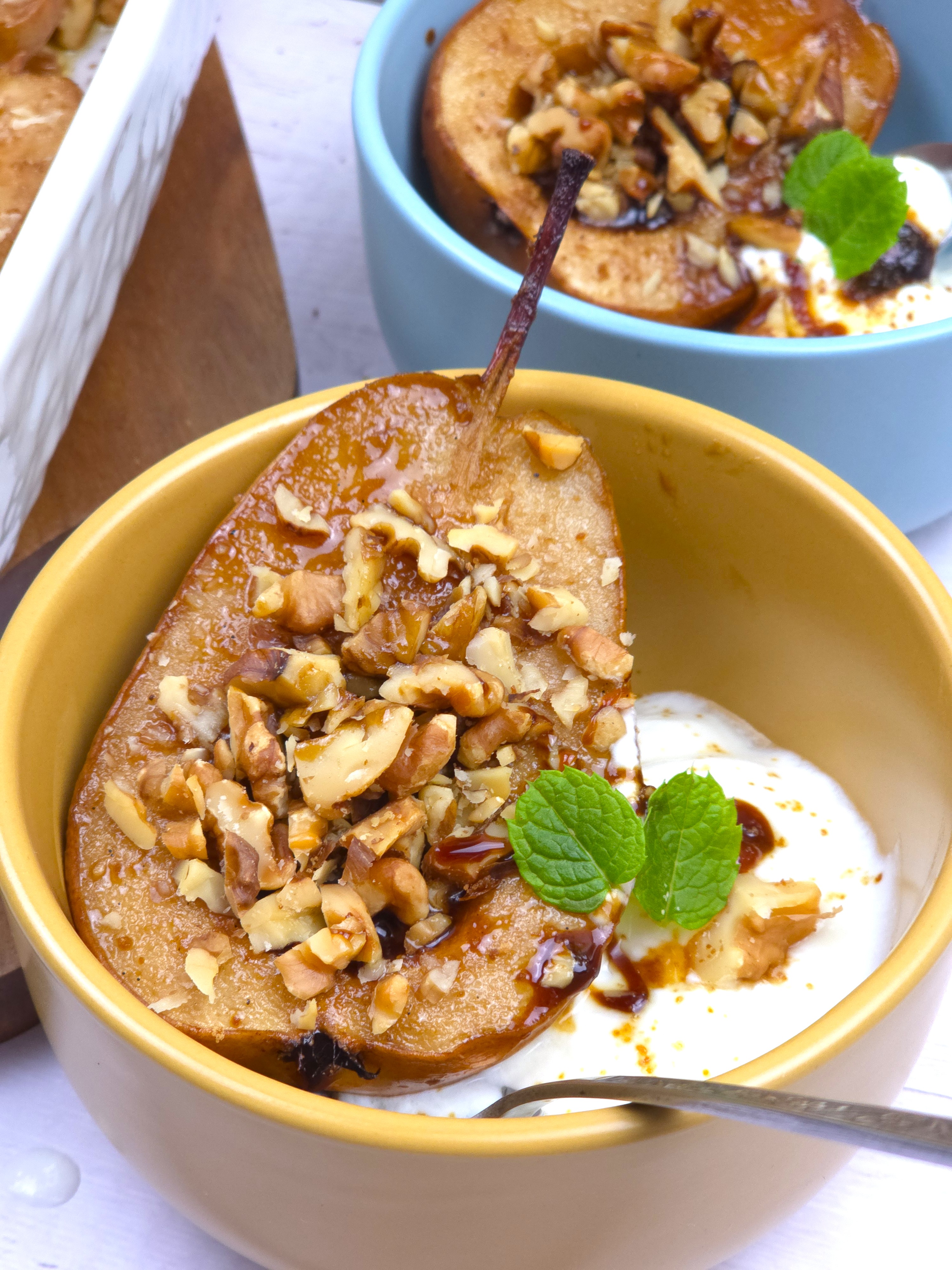 baked pear topped with crushed walnuts in a yellow ceramic bowl with a dollop of homemade yoghurt