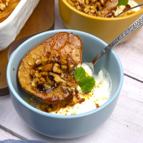 baked pear in a blue bowl with yogurt and spoon