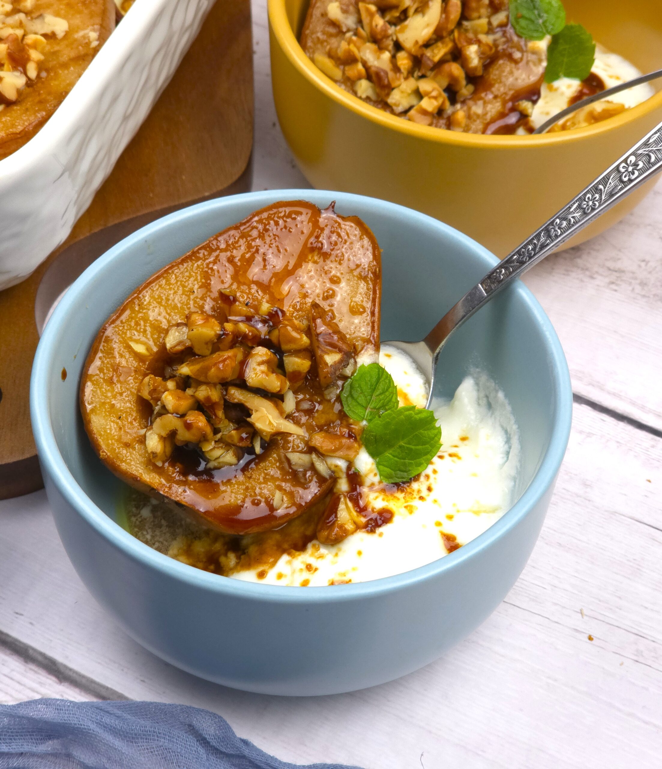 baked pear in a blue bowl with yogurt and spoon