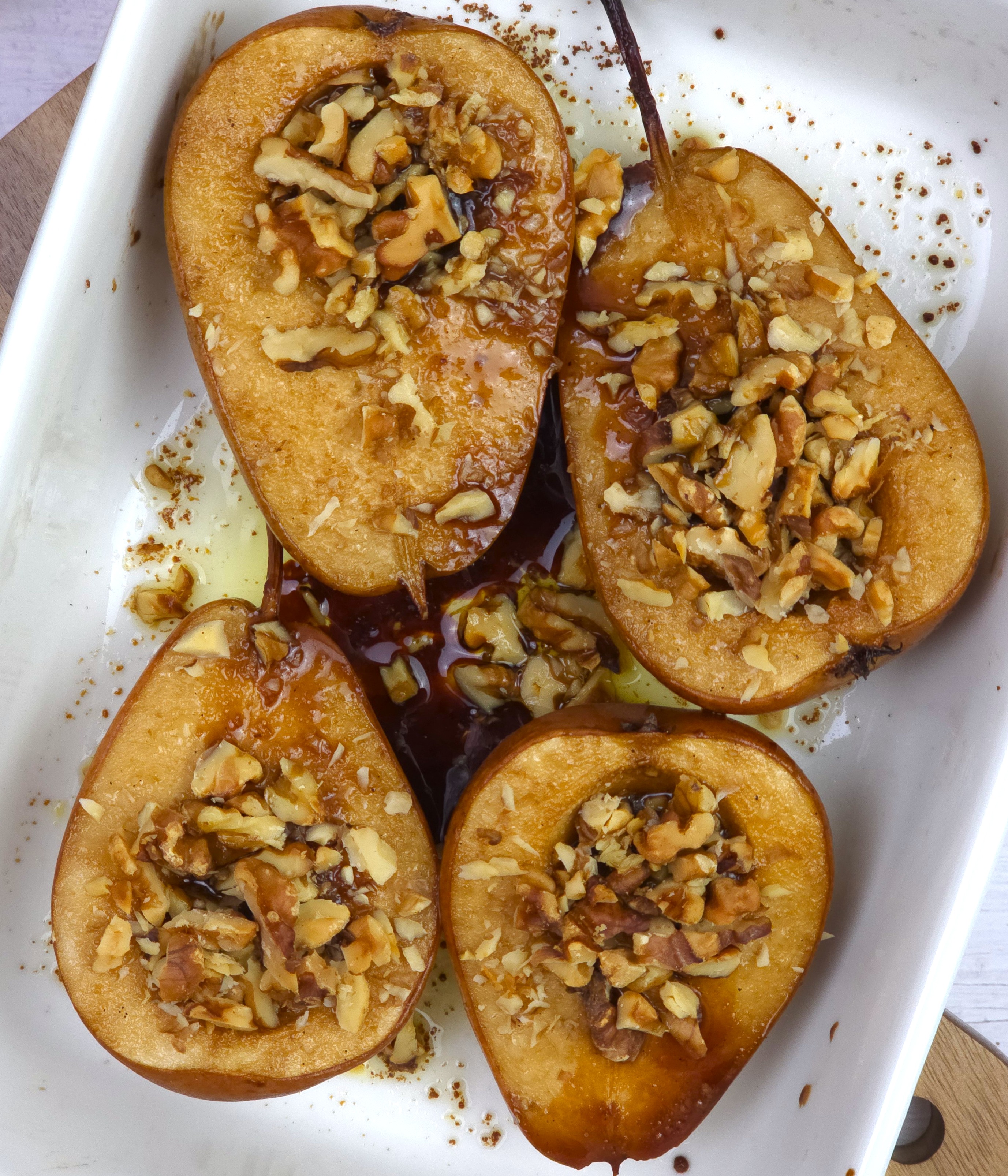 baked pears topped with crushed walnuts in a white ceramic baking dish
