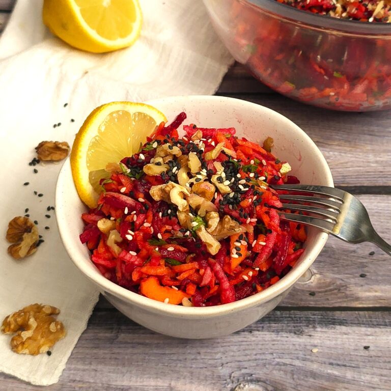 beetroot carrot apple salad in a white stoneware bowl sprinkled with crushed walnuts and sesame seeds
