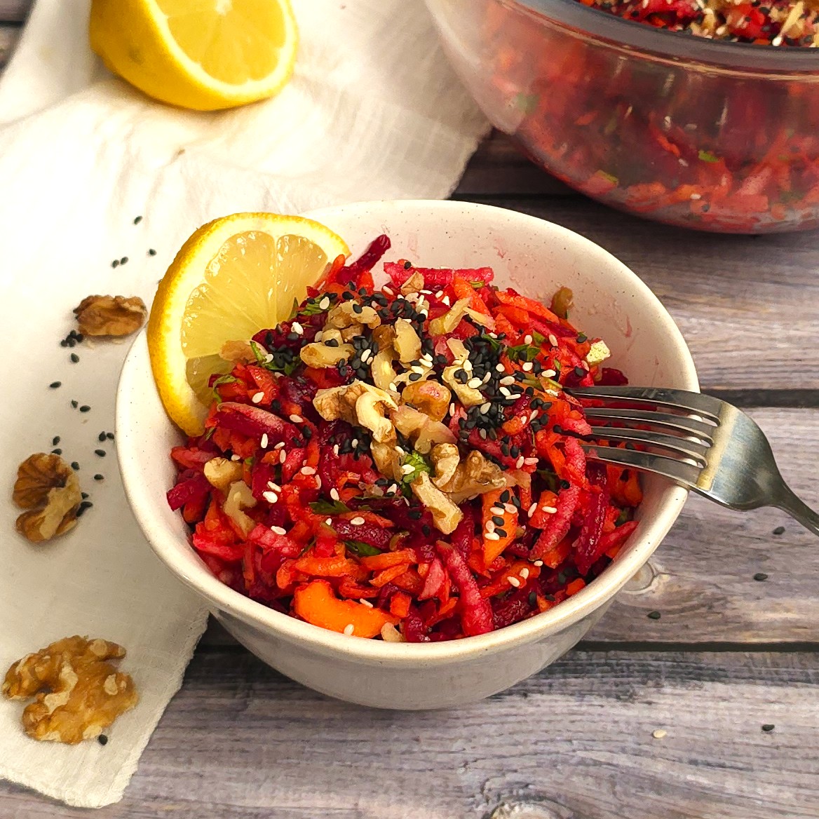 beetroot carrot apple salad in a white stoneware bowl sprinkled with crushed walnuts and sesame seeds