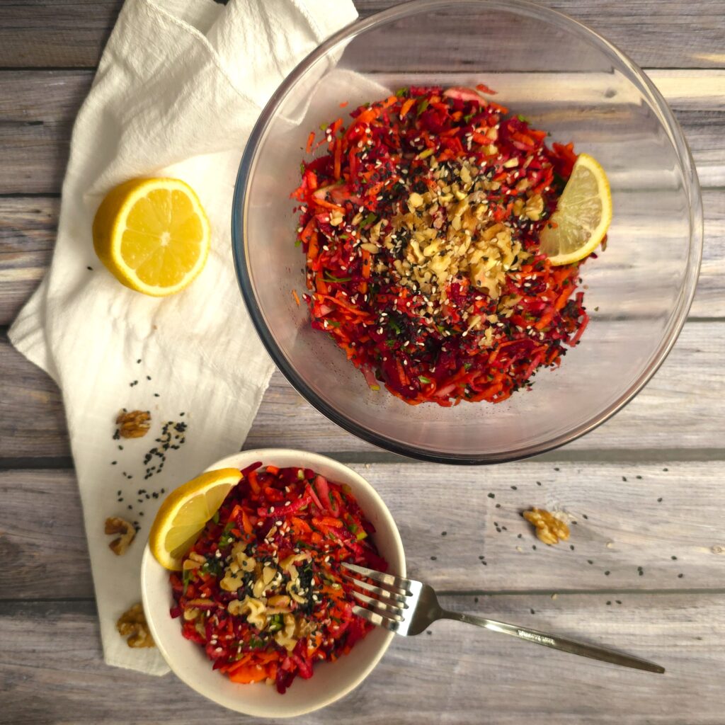 A large glass bowl with beetroot, carrot and apple salad next to a small bowl with salad and fork