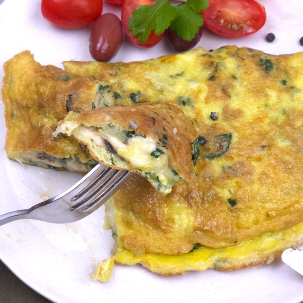 a close look of a kale, mushroom omelette and a bite and fork