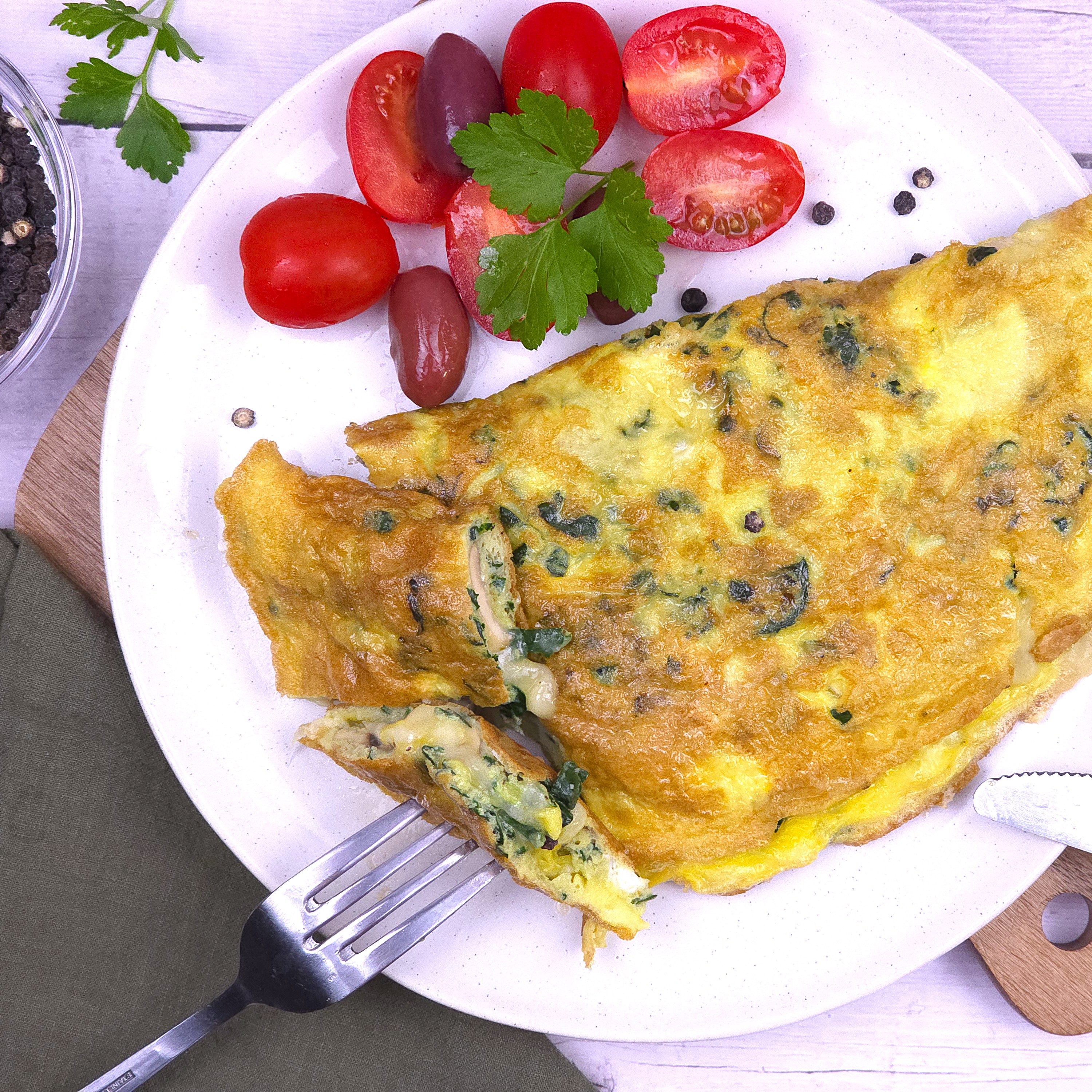 a white stoneware plate with vegetable omelette with cherry tomatoes and kalamata olives