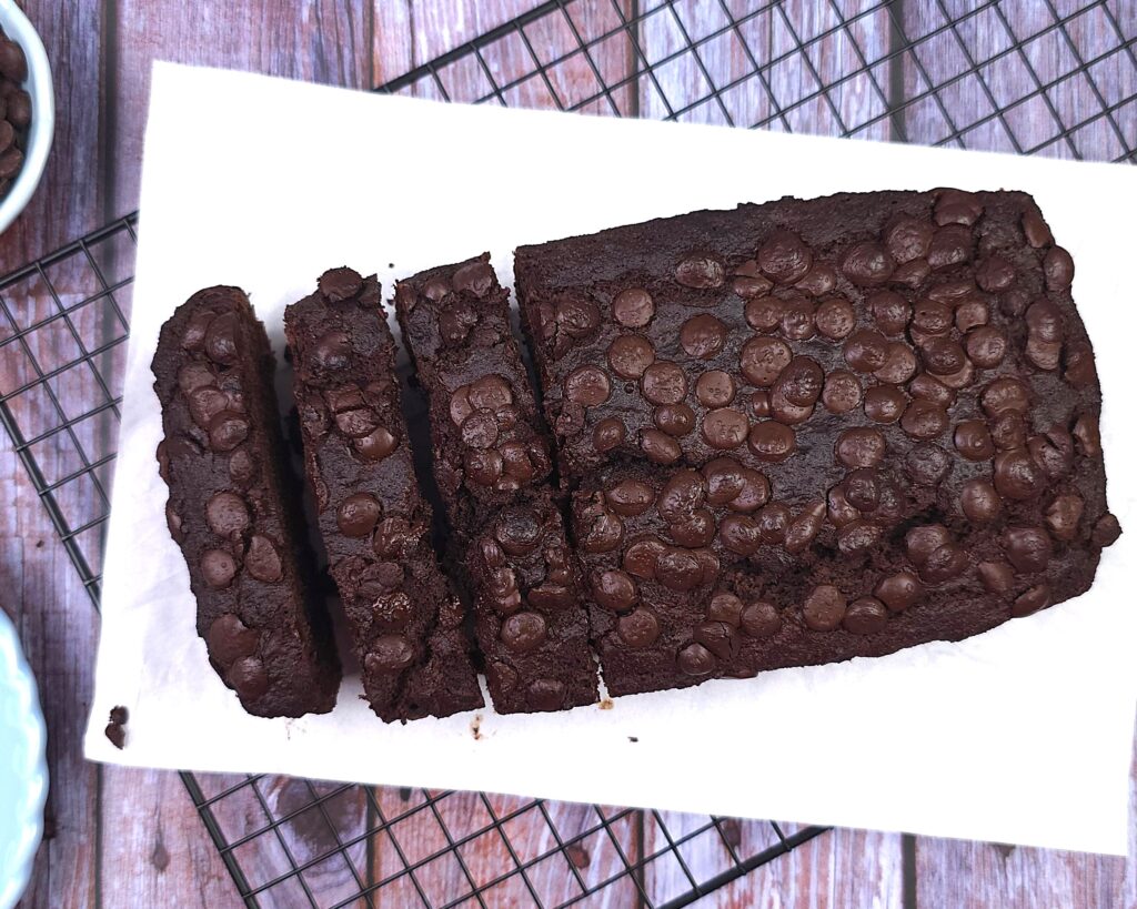 a loaf of gluten-free chocolate banana bread, sliced on a white parchment paper and cooling rack