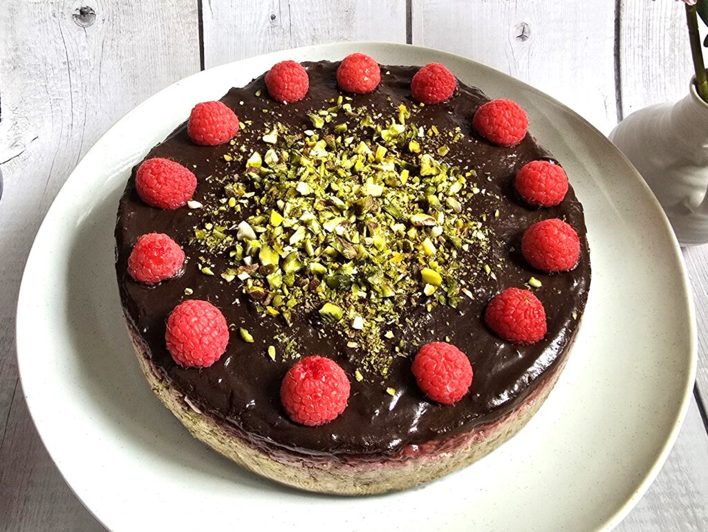 gluten-free no-bake yoghurt tart with avocado chocolate cream topping, decorated with raspberries and pistachios on a ceramic plate.