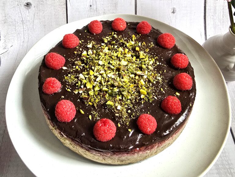 gluten-free no-bake yoghurt tart with avocado chocolate cream topping, decorated with raspberries and pistachios on a ceramic plate.