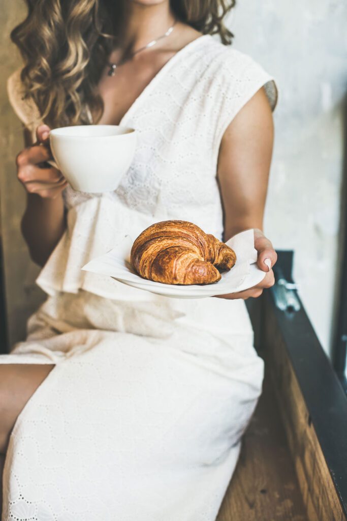 coffee and croissant handed by a women, a gluten-free blogger in white outfit