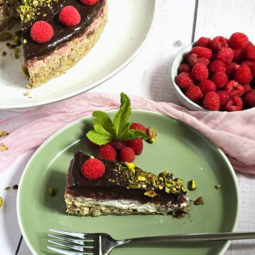 gluten-free no-bake yoghurt tart with avocado chocolate cream topping, decorated with raspberries and pistachios