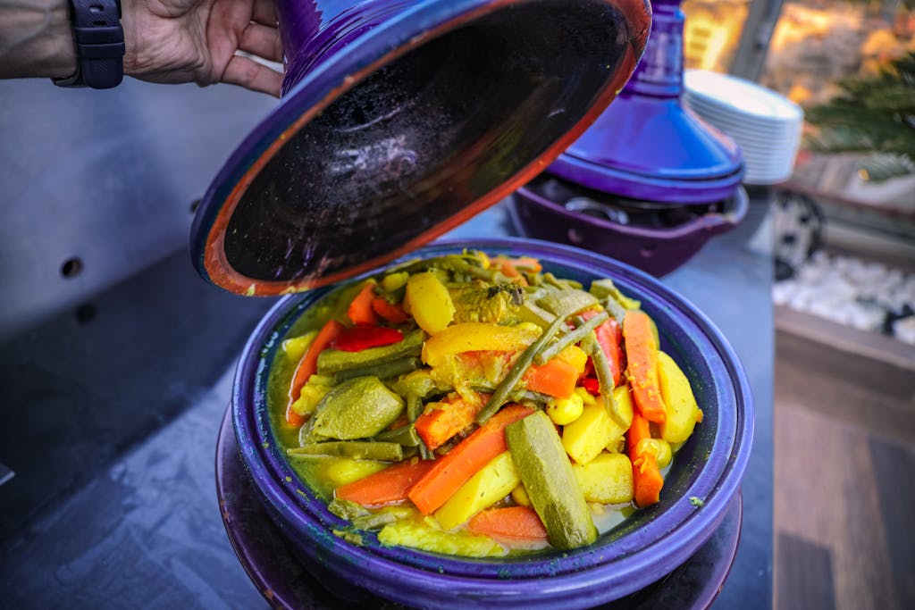 A colorful Moroccan tagine with fresh vegetables being uncovered, showcasing vibrant and healthy cuisine.