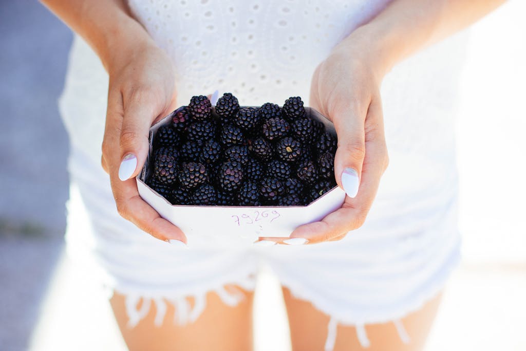 A woman holding a fresh bowl of blackberries on a sunny day, emphasizing healthy eating, like blackberry yoghurt chia parfait