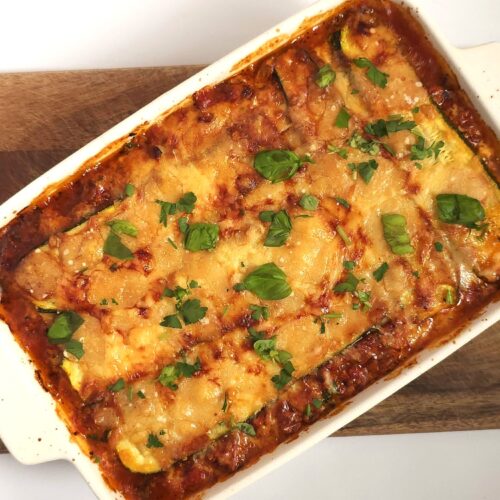 baked healthy zucchini lasagna in a white ceramic baking dish on wooden board
