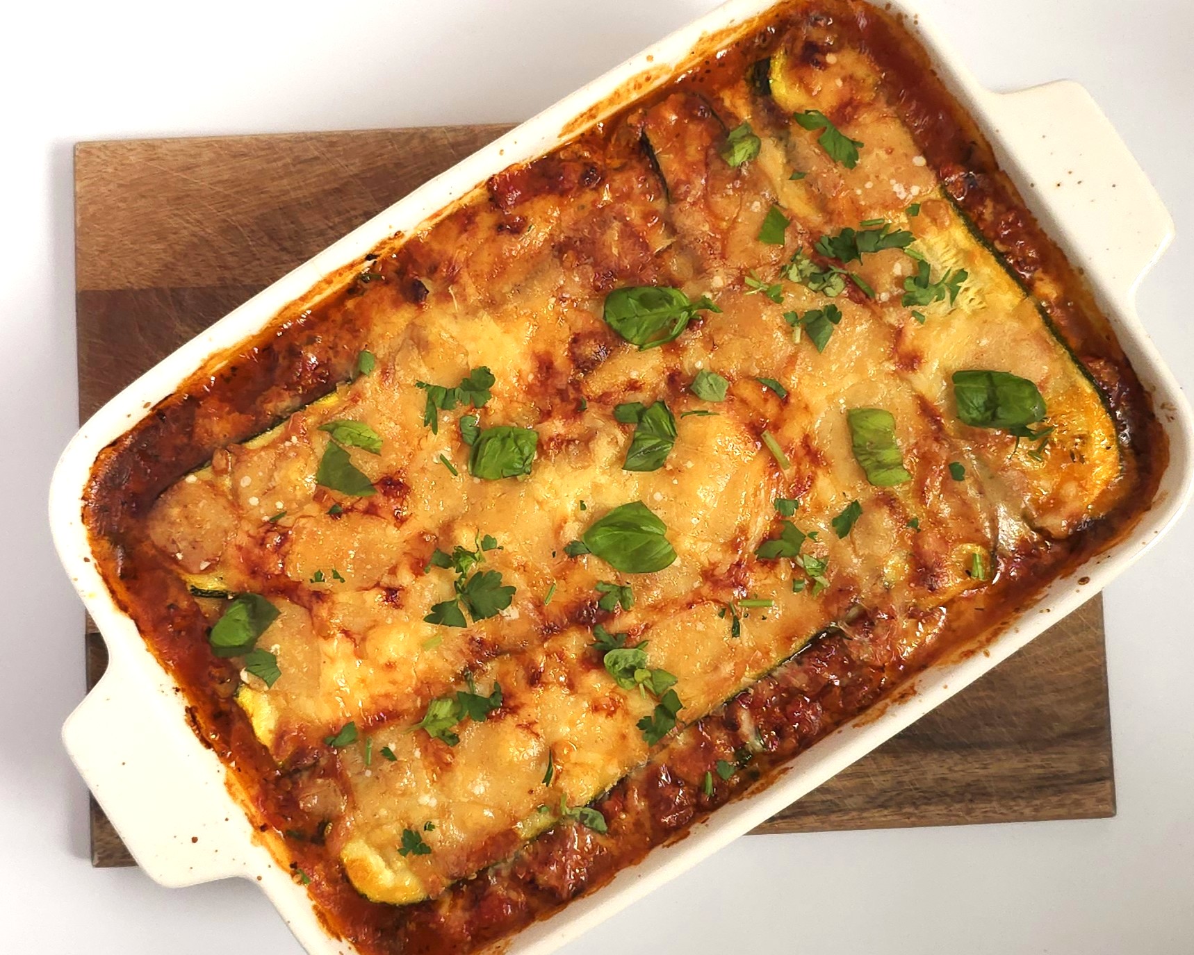 baked healthy zucchini lasagna in a white ceramic baking dish on wooden board