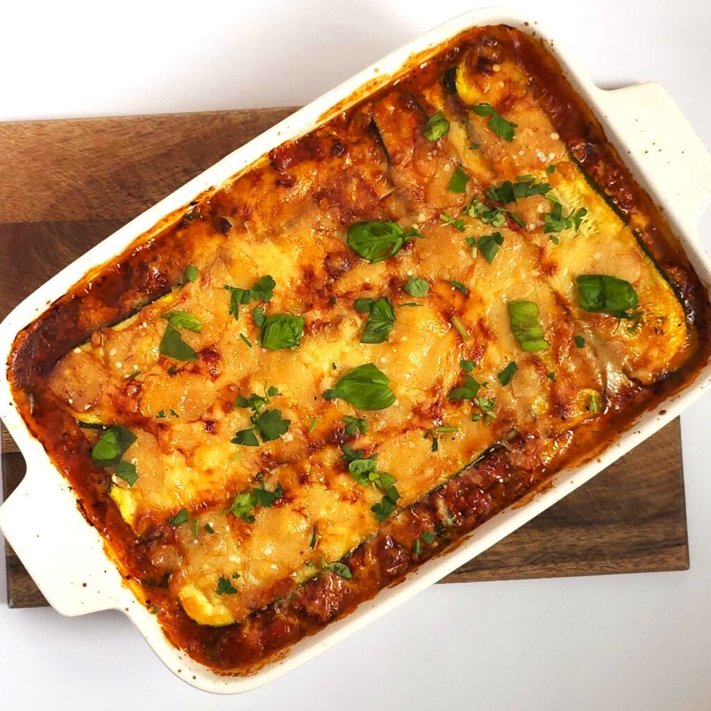 baked healthy zucchini lasagna in a white ceramic baking dish on wooden board