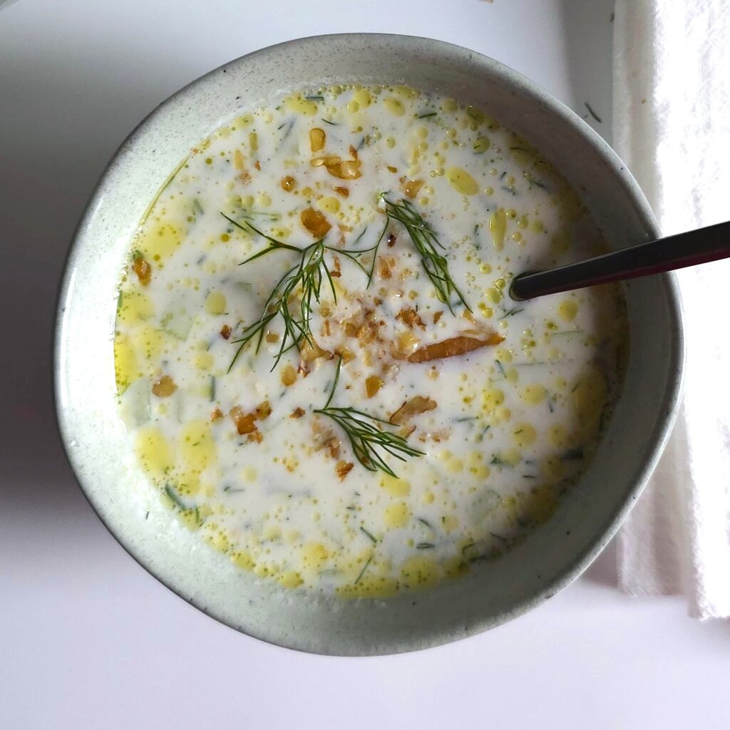 Chilled bowl of traditional Bulgarian tarator soup garnished with crushed walnuts, fresh dill, and a drizzle of olive oil.