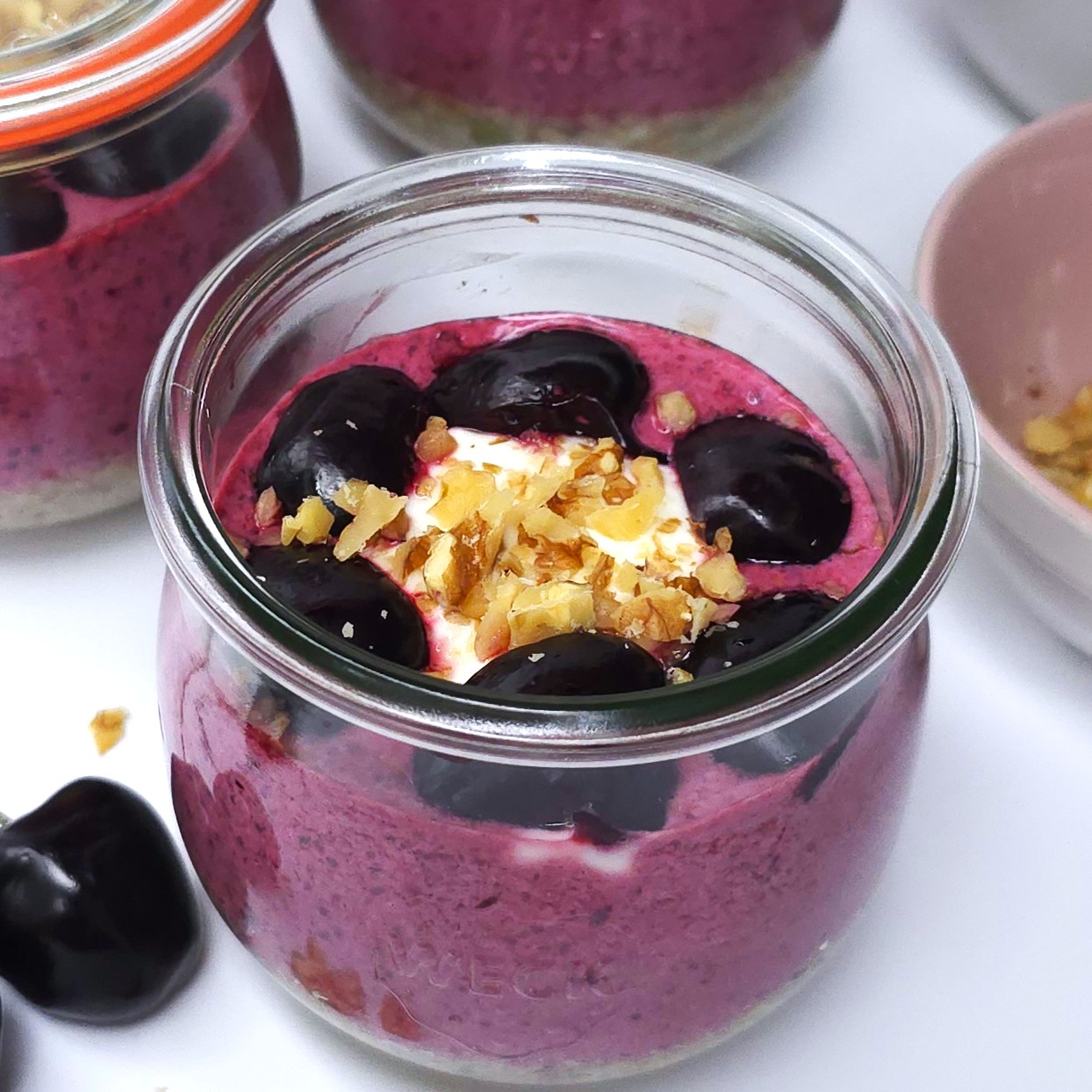 A jar with cherry yoghurt chia parfait topped with halved cherries and crushed walnuts