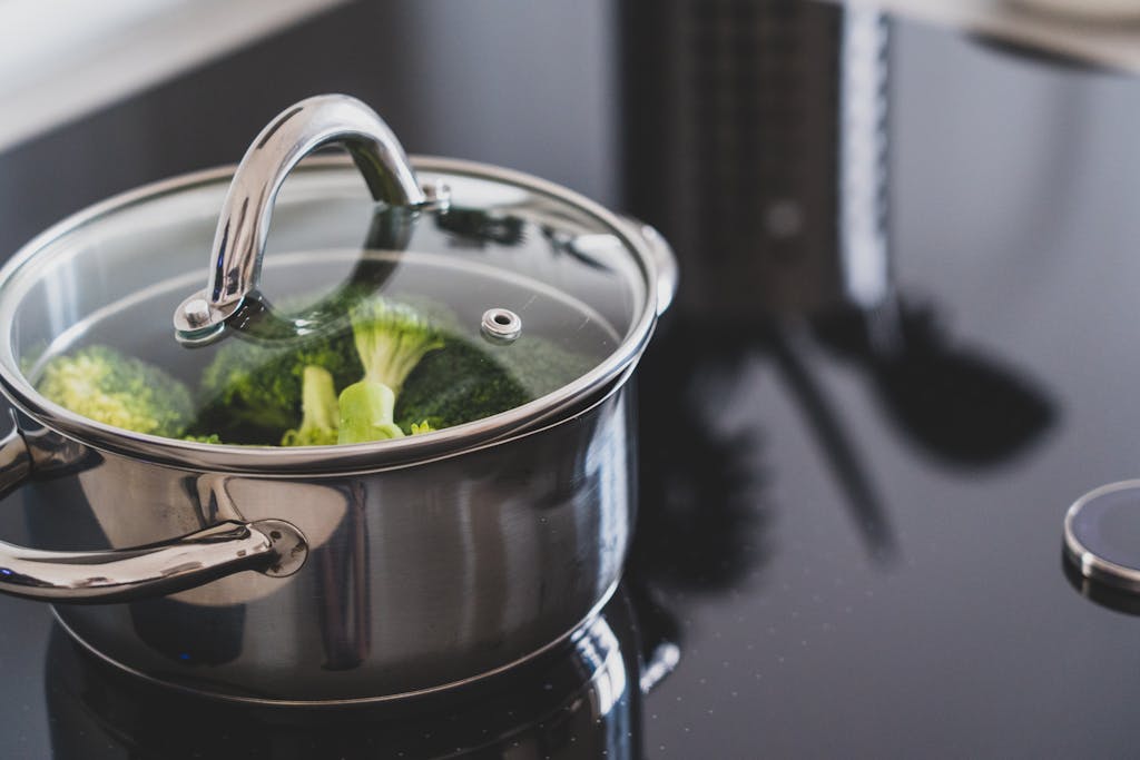 Close-up of broccoli steaming in a stainless steel pot on a modern stovetop indoors.
