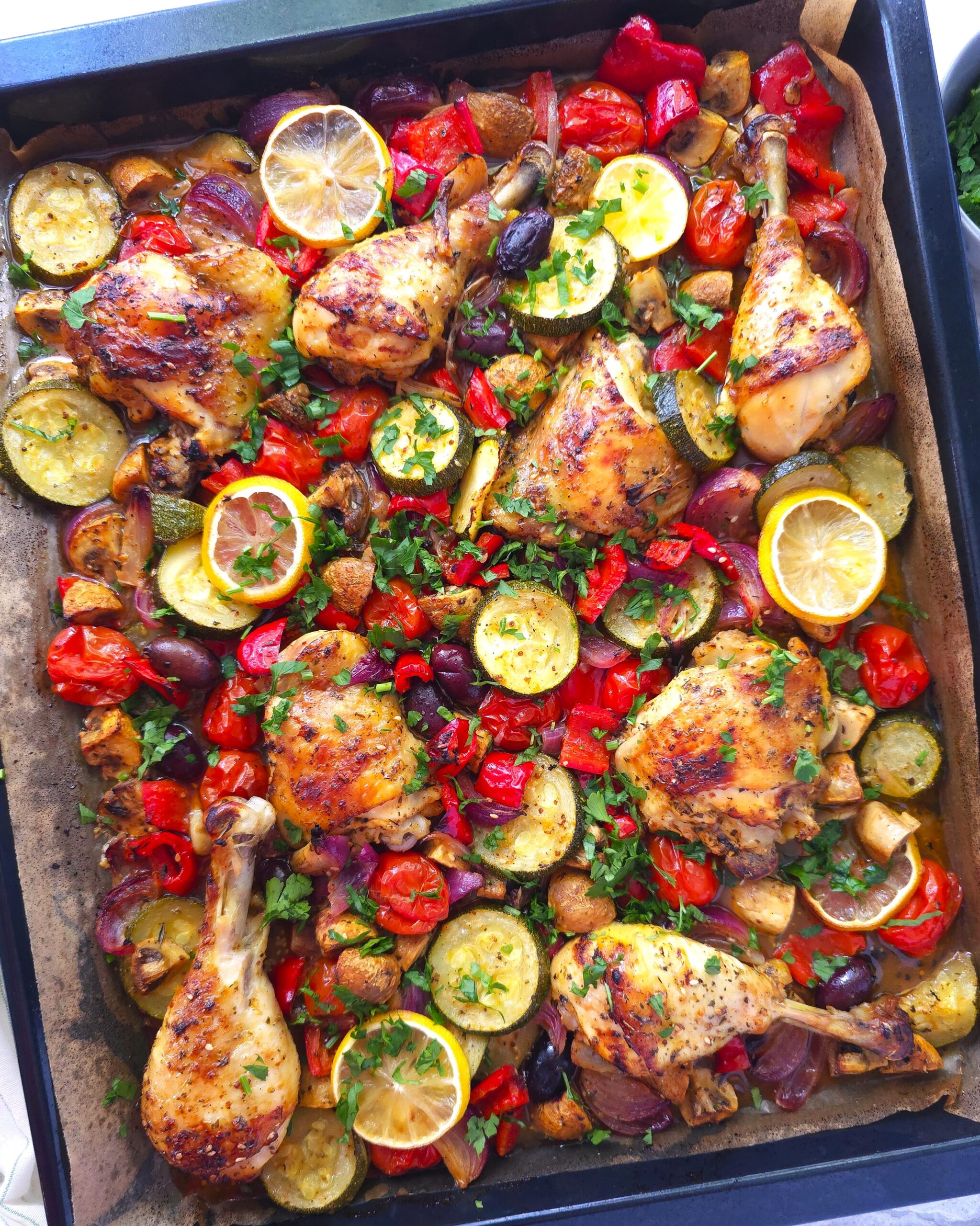 greek sheet pan chicken in a black baking tray