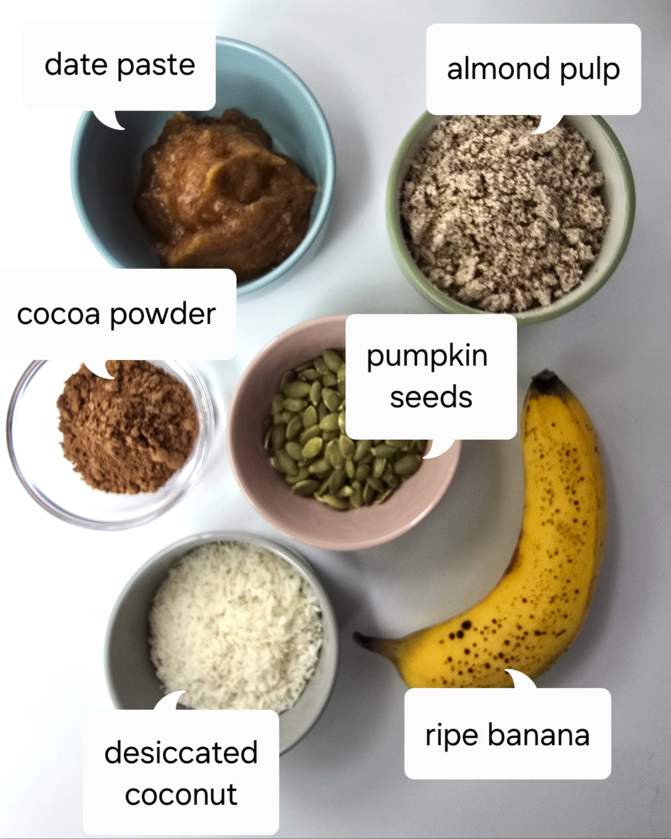 first layer ingredients - almond pulp, date paste, cocoa powder, pumpkin seeds, desiccated coconut  in bowls and ripe banana