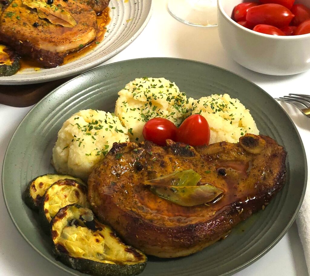 pork chop in a green plate and mash potato and grilled zucchini