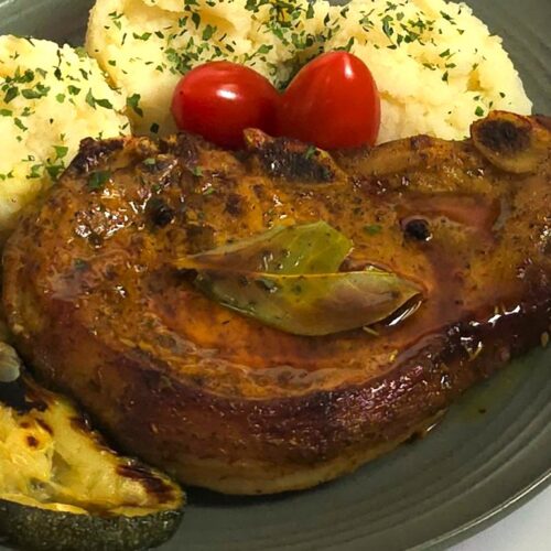 pork chop in a green plate and mash potato and grilled zucchini