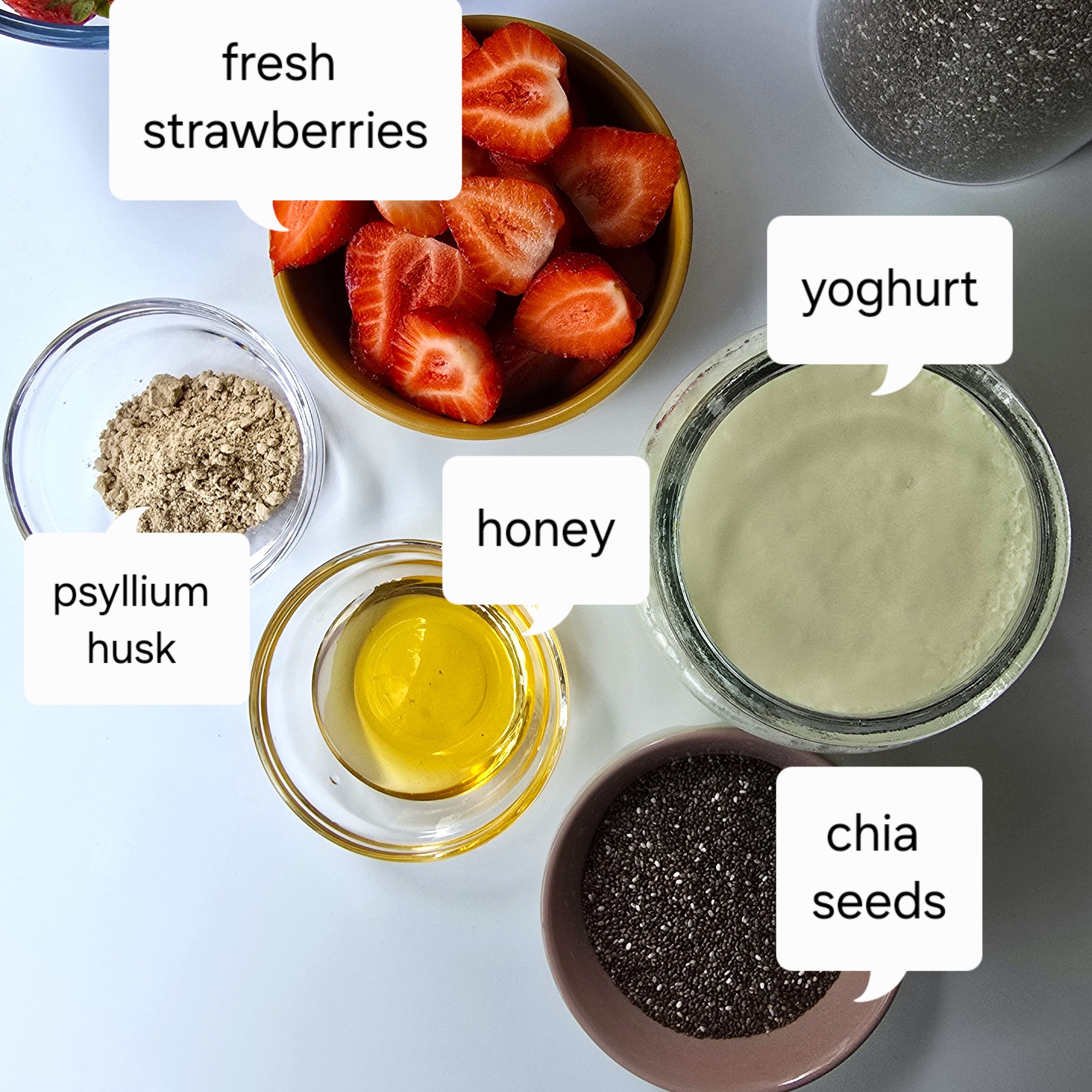 second layer ingredients - fresh halved strawberries, chia seeds, psyllium husk powder, honey in bowls and a jar with homemade yoghurt