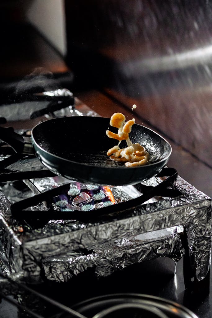 Shrimp being tossed in a frying pan on a gas stove, showcasing culinary skill.
