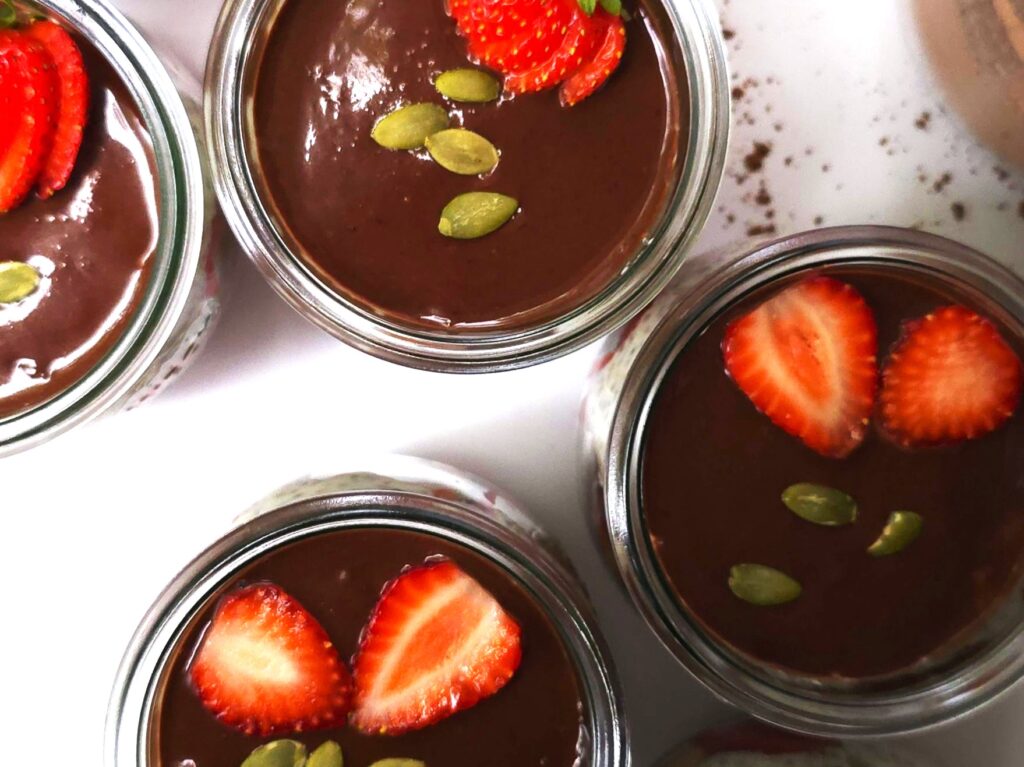 strawberry yoghurt chia parfait in jars with chocolate ganache, decorated with sliced strawberries and pumpkin seeds on the top