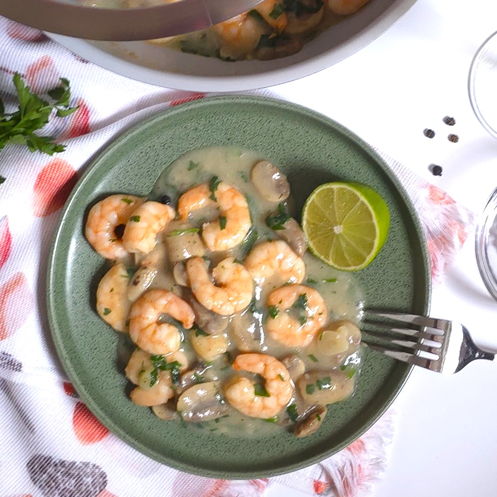 a green plate with a garlicy mushroom prawns, fork and half lime