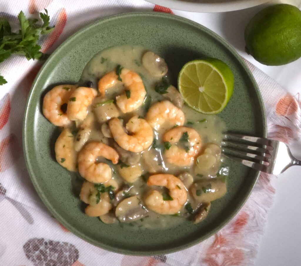 a green plate with a garlicy mushroom prawns, fork and half lime