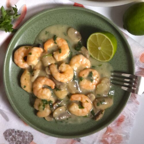 a green plate with a garlicy mushroom prawns, fork and half lime