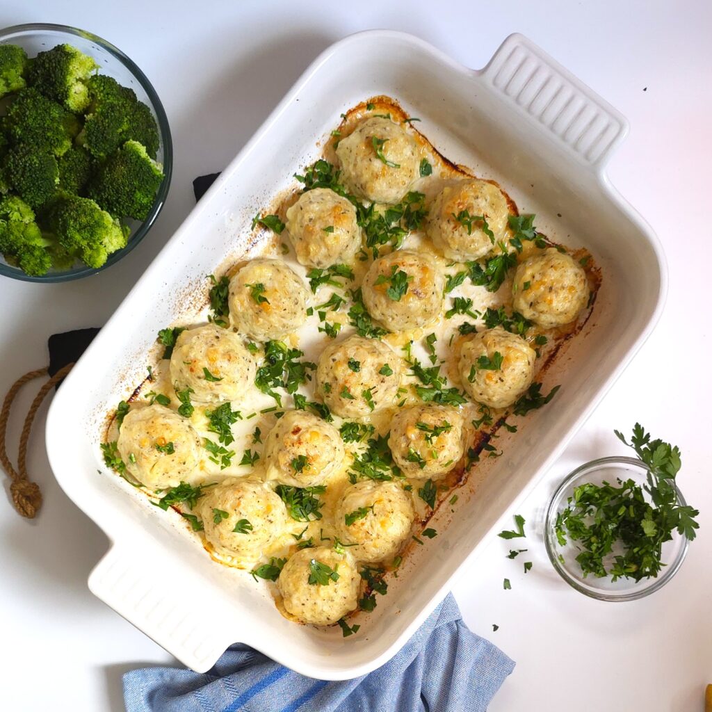 cheesy chicken meatball recipe in a white ceramic baking ray, spincled with chopped parsley