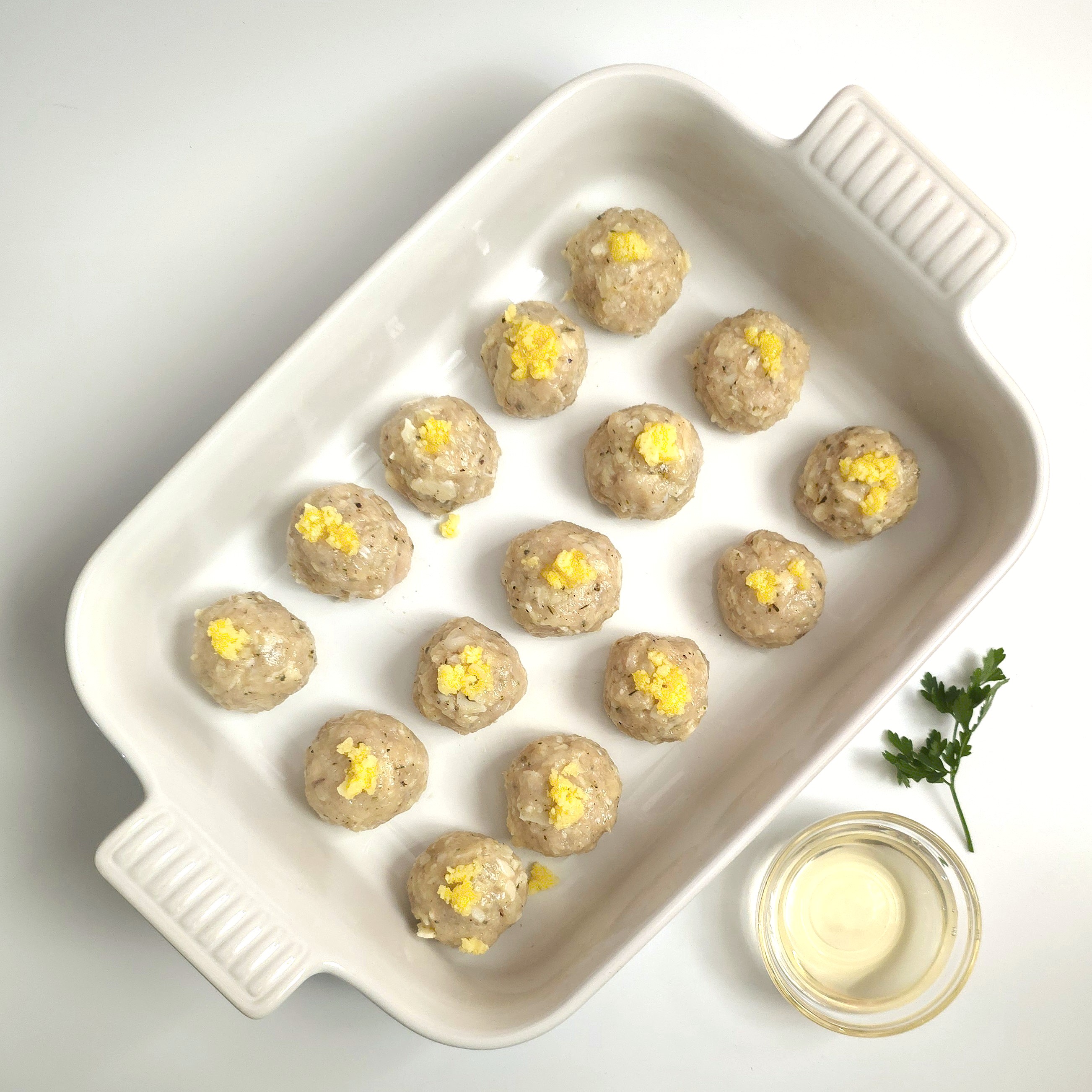 a white ceramic baking dish with shaped cheesy meatballs with ghee butter on top and a small bowl with white wine
