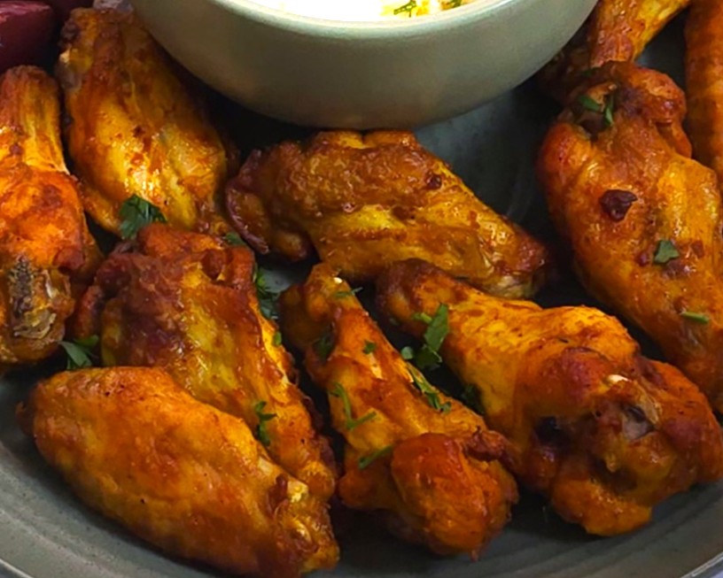 a close look of chicken wings in a green plate next to yoghurt garlic sauce dip in a green bowl