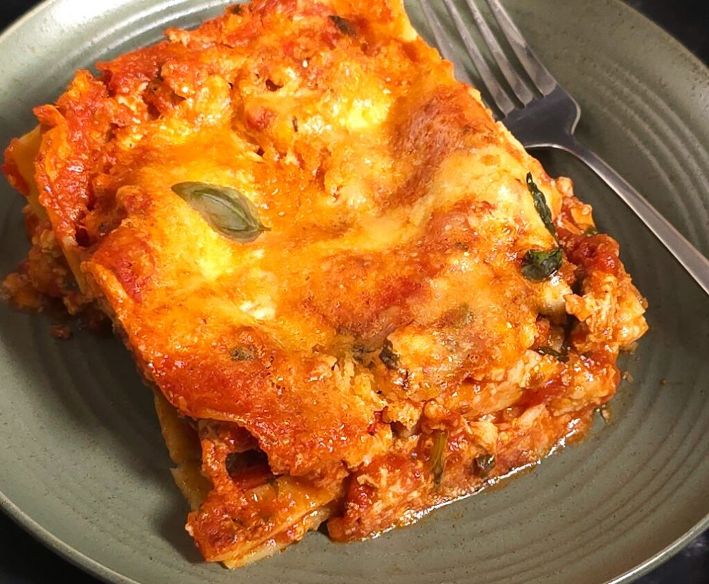 a close look of a square of gluten-free, lactose-free lasagna in a green plate and fork