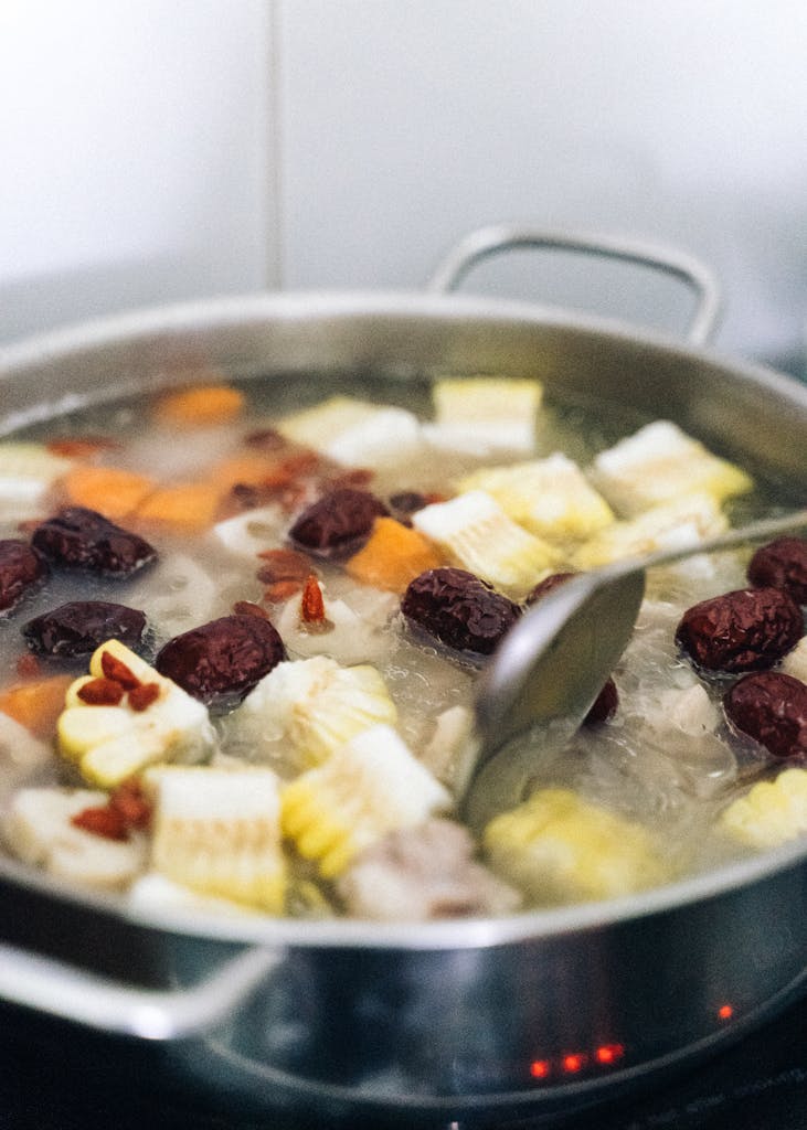 Close-up of a pot filled with boiling soup, featuring corn cobs, spices, and hearty ingredients.