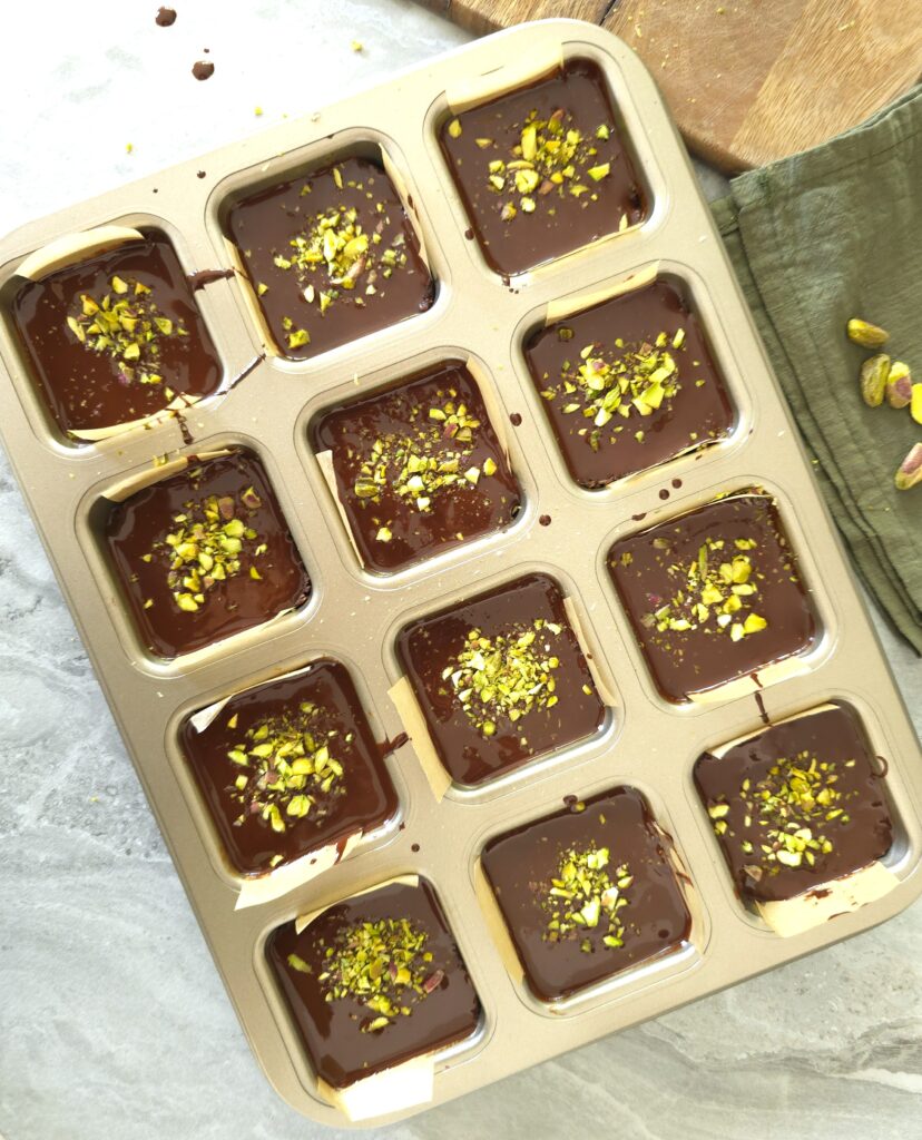 nut bars in a tin, covered with melted chocolate and sprinkled with crushed pistachio