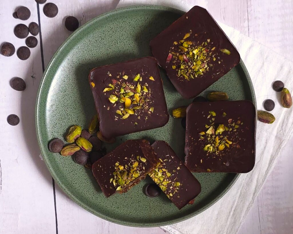 a few date pistachio chocolate bars in a green plate and sprinkled chocolate chips and pistachios