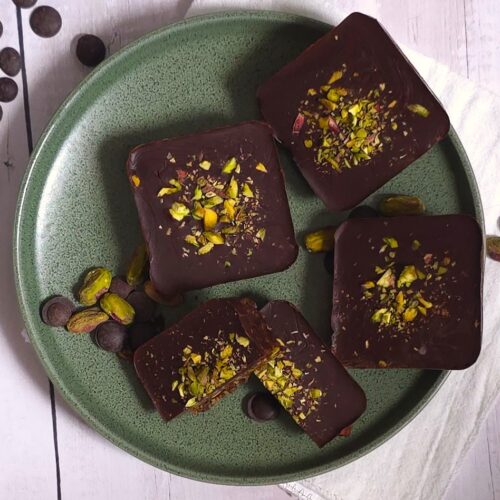 a few date pistachio chocolate bars in a green plate and sprinkled chocolate chips and pistachios