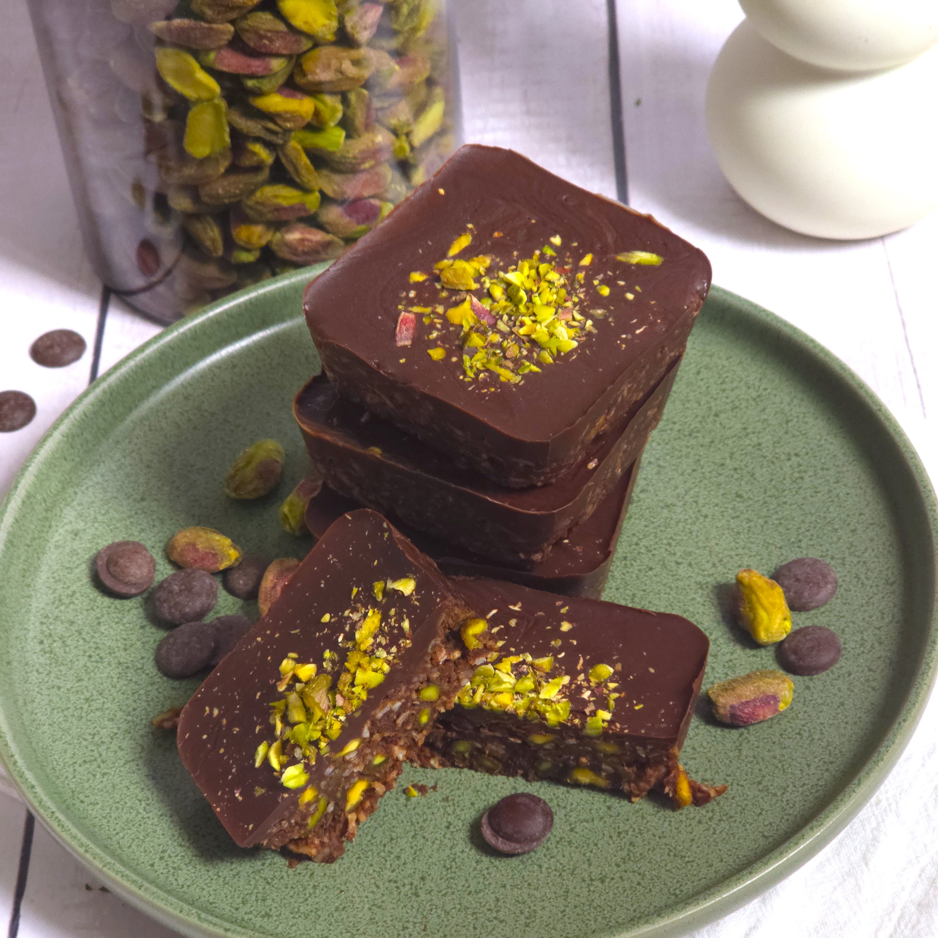 Healthy no-bake pistachio chocolate bars topped with crushed pistachios, served on a plate